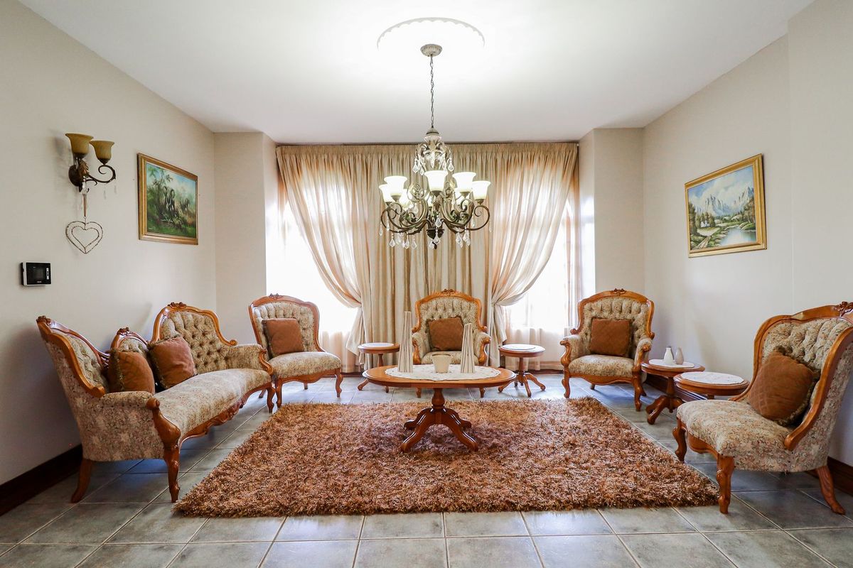 A formal living room featuring tiled flooring, a decorative ceiling rose with a chandelier, and arched entryways, creating a classic and structured living space.