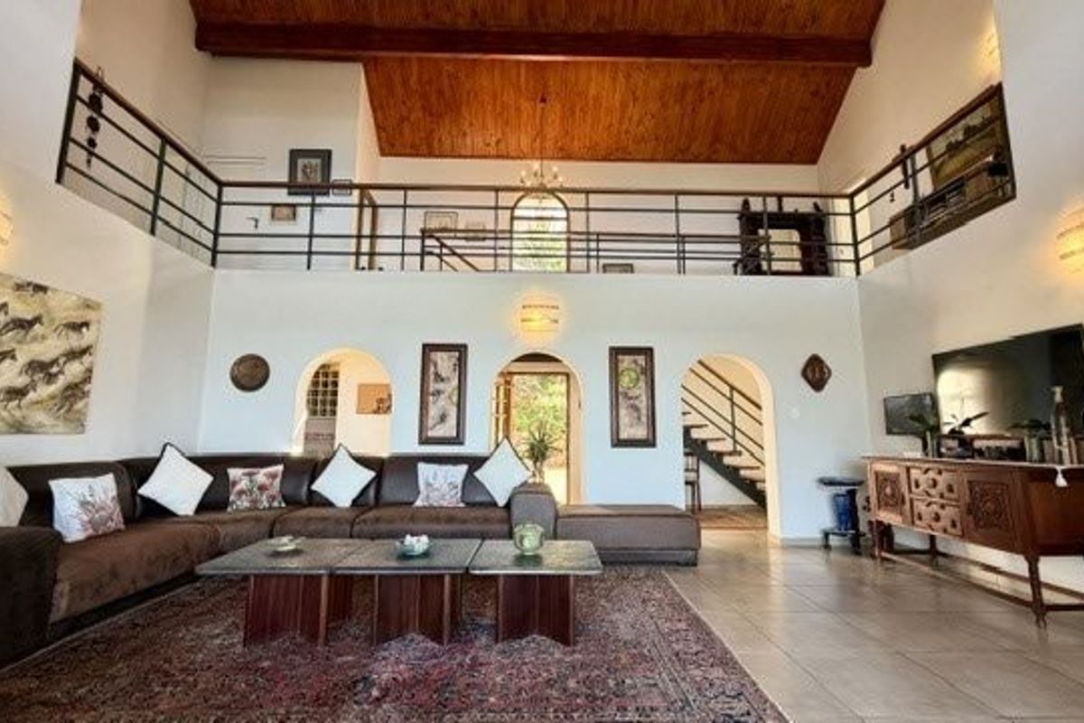 Spacious double-volume living room featuring a vaulted timber ceiling, mezzanine level with metal balustrade, and arched architectural details leading to adjacent areas.