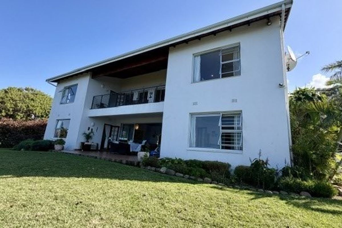 Rear view of a two-story residential house featuring a balcony, tiled patio area, and well-maintained lawn.
