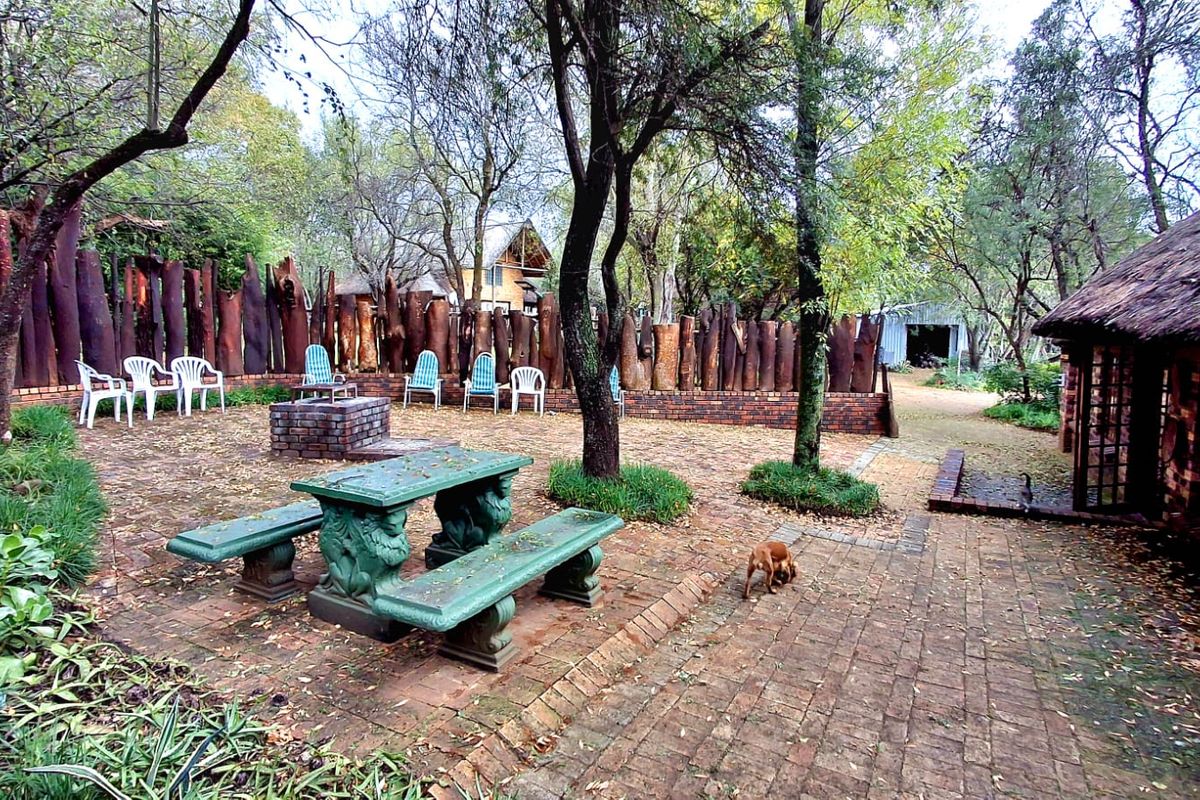 Outdoor patio area featuring brick paving, a built-in brick fire pit, and a rustic log boundary fence adjacent to a thatched building.