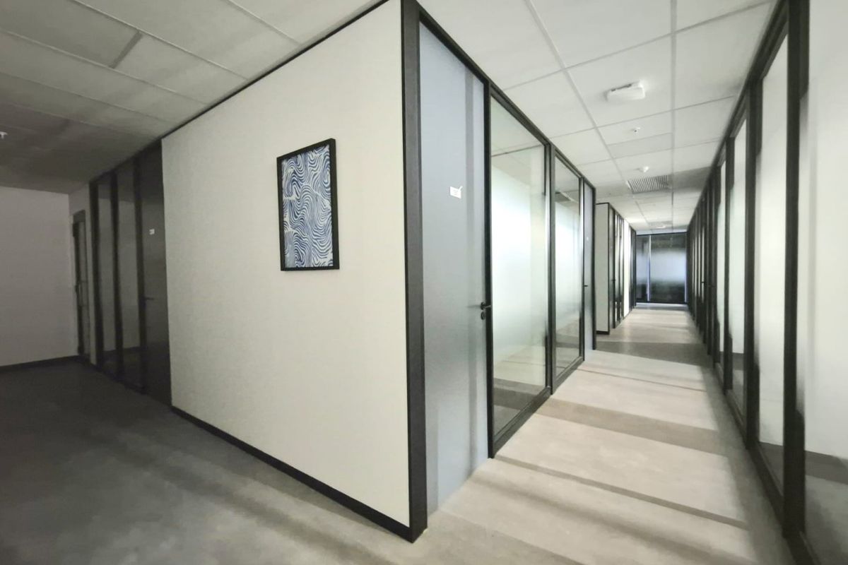A modern commercial office hallway featuring glass partition walls, suspended ceilings, and polished concrete flooring, providing a clean and professional workspace layout.