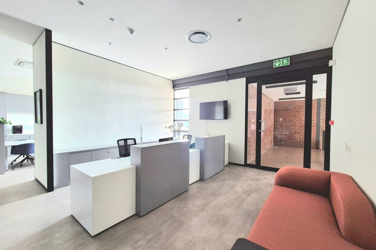 Modern commercial office reception area featuring a built-in reception desk, recessed lighting, and a glass door leading to an adjacent workspace.