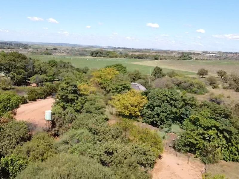 Aerial view of the farm property featuring expansive green fields, mature trees, a dirt access road, and a water tank.