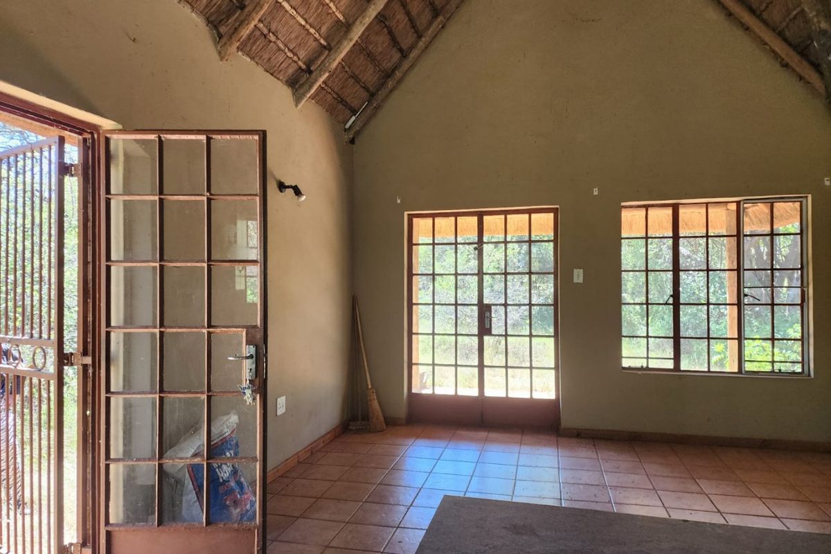Spacious living area featuring a traditional thatched roof with exposed rafters, terracotta tiled flooring, and large steel-framed windows providing natural light and garden views.