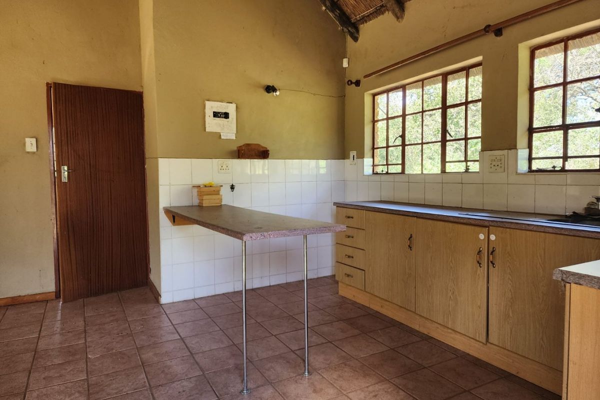 A rustic kitchen featuring tiled flooring, laminate cabinetry, a tiled backsplash, and a traditional thatched roof ceiling with natural light.