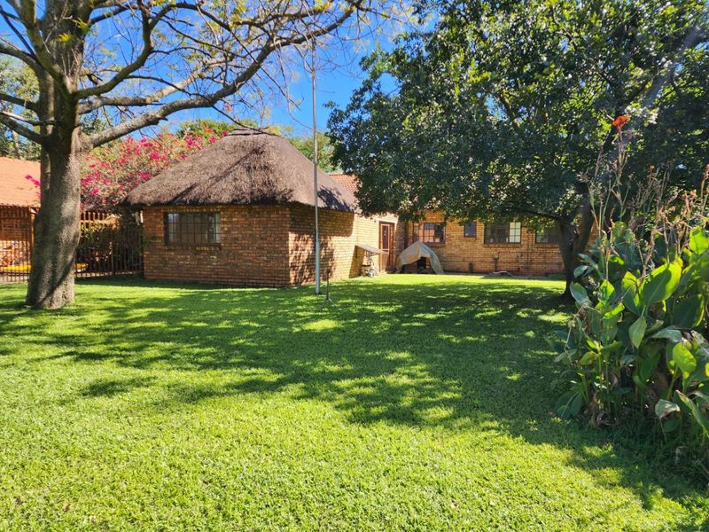 A rear view of a farm-style property featuring a traditional thatched roof, face brick construction, and a well-maintained garden area.