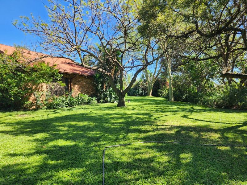 A spacious, well-maintained garden area featuring mature trees and a lush lawn, adjacent to the brick exterior of the farm property.