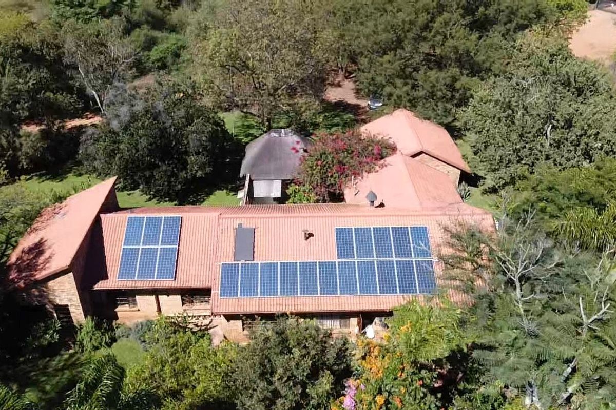 Aerial view of a farm property featuring a large tiled roof with an extensive solar panel installation set within a lush, wooded landscape.