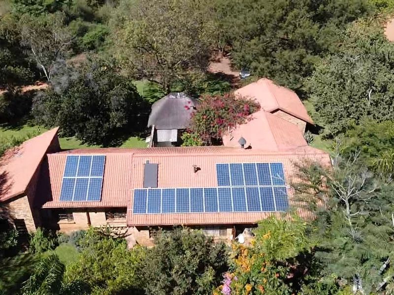 Aerial view of a farm property featuring a large tiled roof with an extensive solar panel installation set within a lush, wooded landscape.