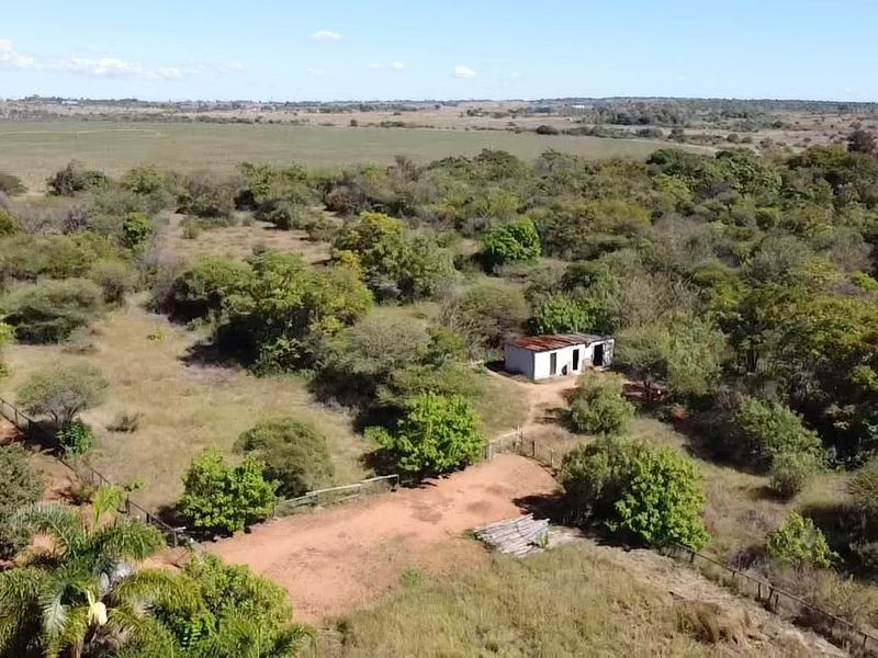Aerial view of a rural farm property featuring expansive natural landscape, a dirt driveway, perimeter fencing, and a small, weathered outbuilding.