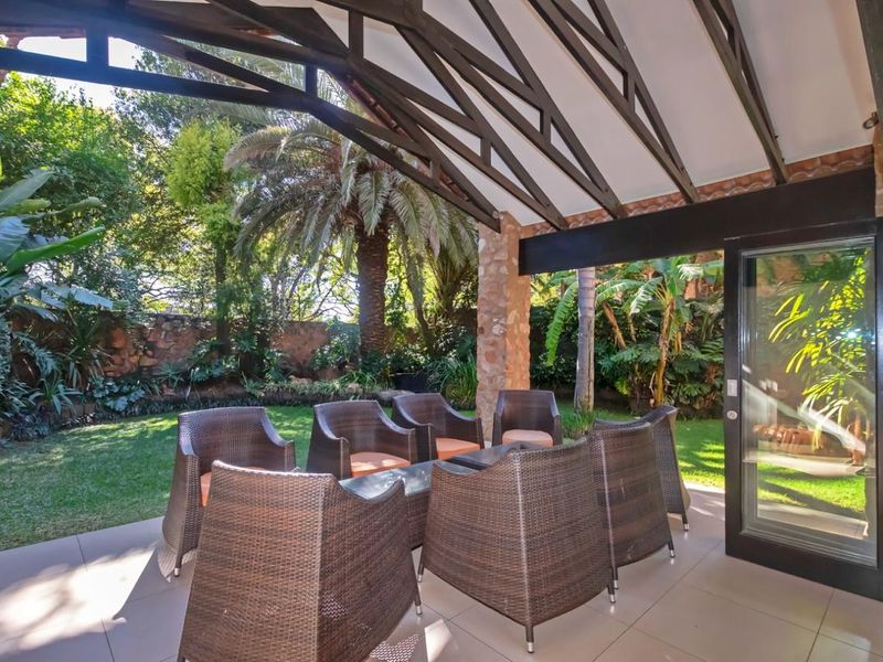 A covered patio featuring exposed timber roof trusses, tiled flooring, and a stone-clad pillar, providing seamless access to the lush garden.