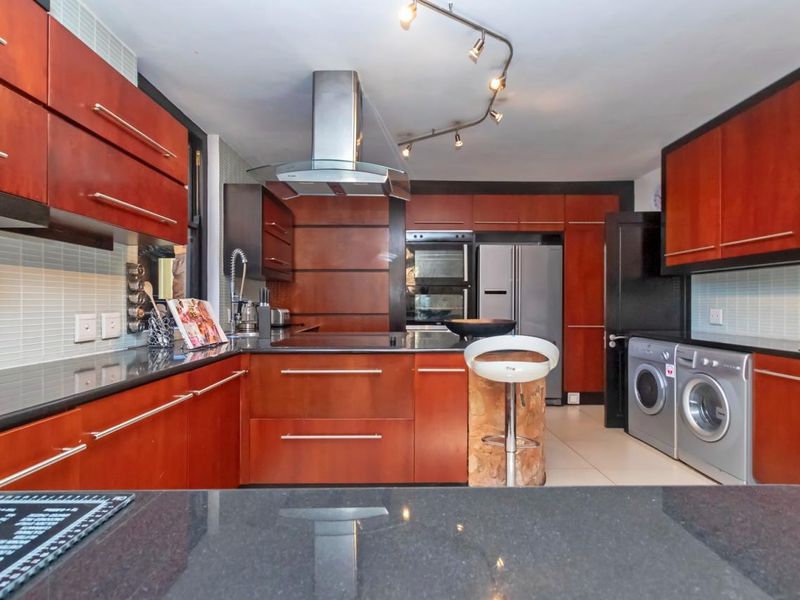 A functional kitchen featuring dark wood cabinetry, granite countertops, integrated appliances, and a tiled backsplash with modern track lighting.