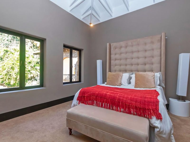 Spacious bedroom featuring a high vaulted ceiling with exposed rafters, neutral wall tones, and large casement windows providing natural light.