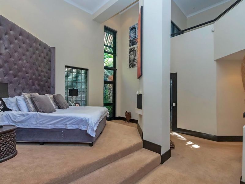 Spacious bedroom featuring a raised sleeping platform, high ceilings, and tall vertical windows that provide natural light and garden views.