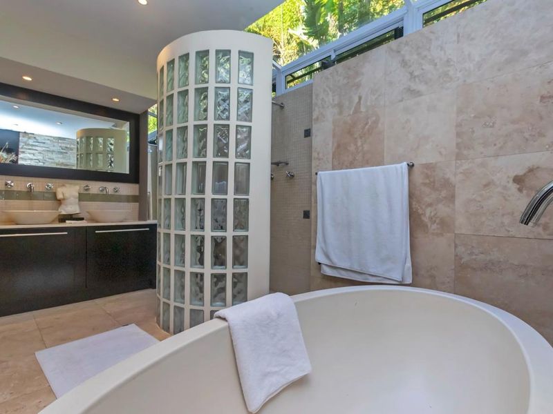 Modern bathroom featuring a freestanding bathtub, a unique glass block shower enclosure, double vanity with vessel sinks, and natural stone wall tiling.
