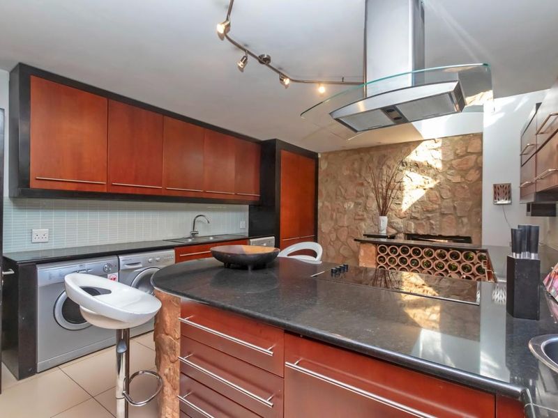 Modern kitchen featuring dark wood cabinetry, a stone feature wall, a central island with a built-in hob, and integrated appliances.