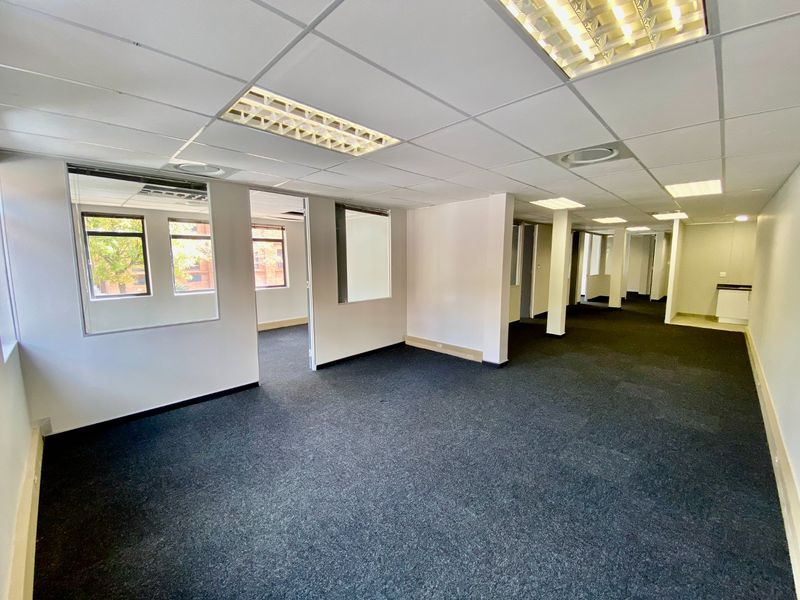 An open-plan commercial office space featuring suspended ceilings, recessed lighting, carpeted flooring, and internal glass partitions, offering a versatile layout for business operations.