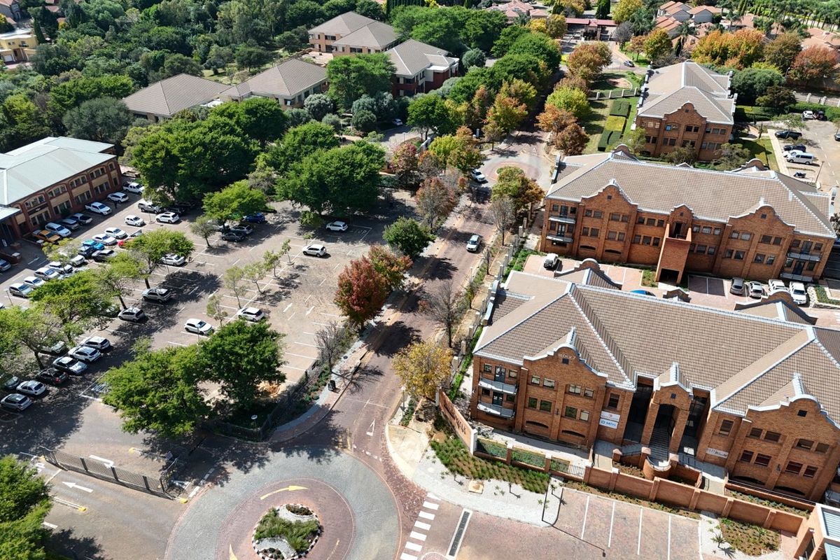 Aerial view of a commercial office park featuring brick buildings, extensive paved parking, landscaped grounds, and a central roundabout.