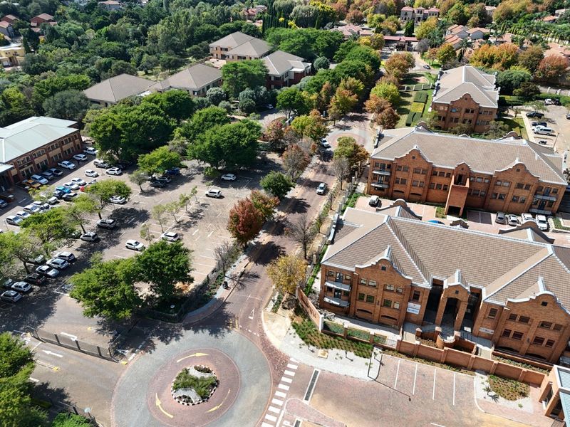 Aerial view of a commercial office park featuring brick buildings, extensive paved parking, landscaped grounds, and a central roundabout.