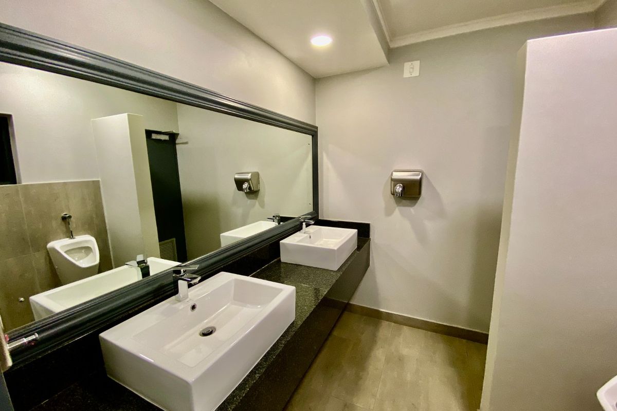 Modern commercial bathroom featuring a dual vessel sink vanity with granite countertop, large framed mirror, and wall-mounted fixtures.