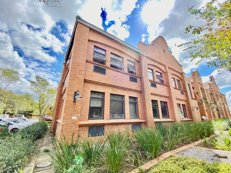 A well-maintained commercial building featuring a classic face brick facade, large casement windows, and established garden landscaping.