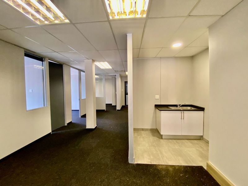Open-plan commercial office space featuring a kitchenette area, glass partitioning, suspended ceilings, and carpeted flooring throughout.