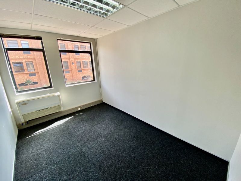 A clean, empty office space featuring carpet tiles, a suspended ceiling with recessed lighting, and a wall-mounted air conditioning unit.