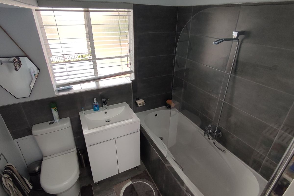 Modern bathroom featuring a white vanity, toilet, and a bathtub with a glass shower screen and dark grey wall tiling.