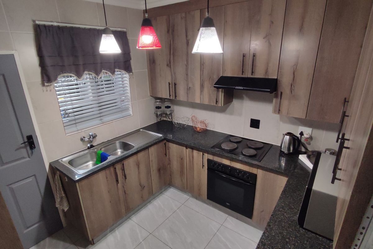 Modern kitchen featuring wood-look cabinetry, granite countertops, built-in oven, electric hob, extractor fan, and a stainless steel double sink with tiled finishes.