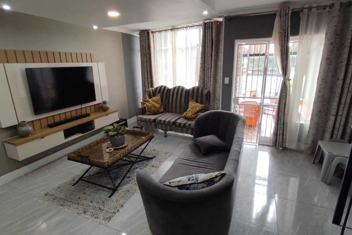 A well-maintained living room featuring tiled flooring, recessed lighting, and a modern built-in media unit with direct access to an outdoor patio area.
