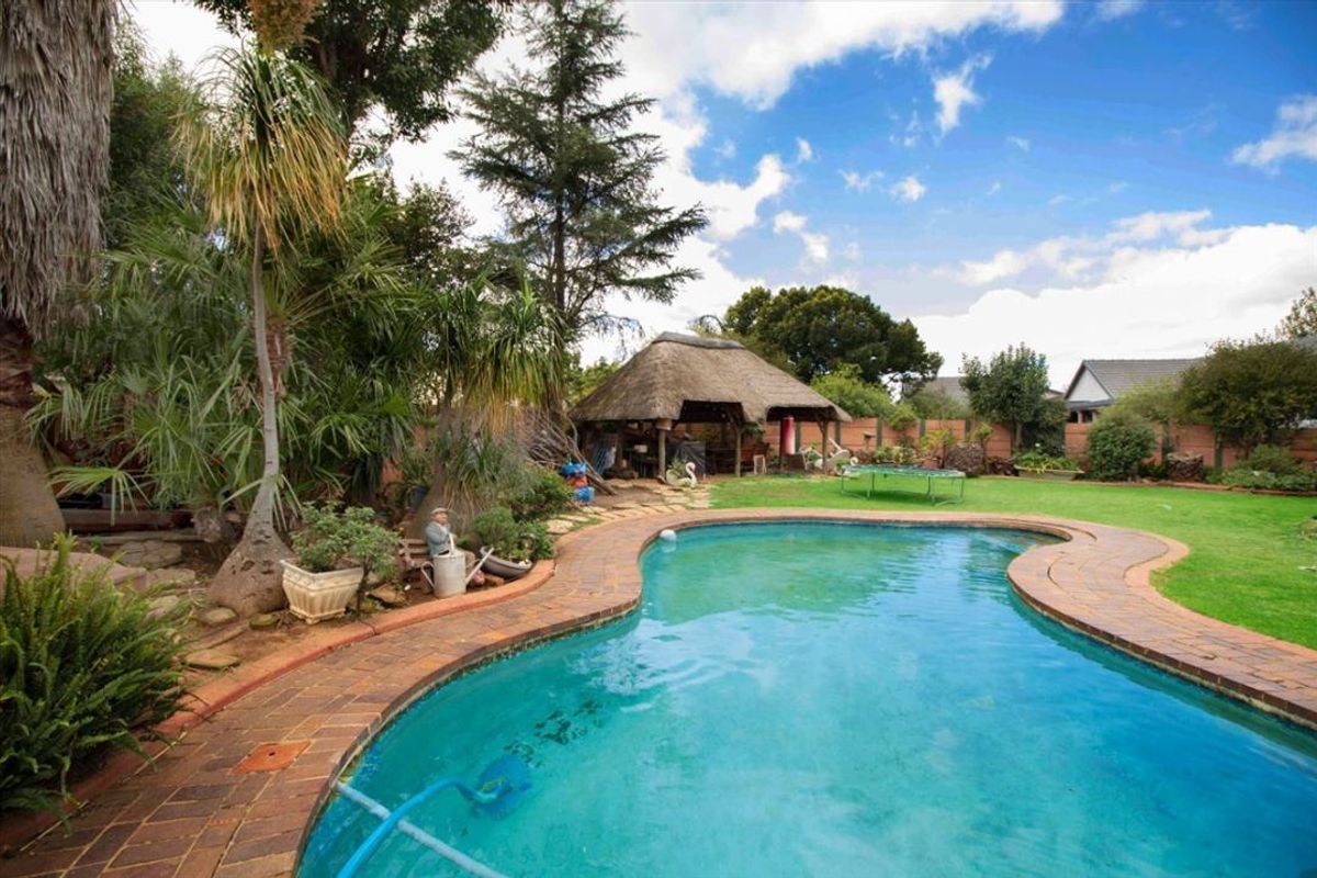 Outdoor pool area featuring a swimming pool with brick coping, a thatched lapa, and a spacious lawn garden.