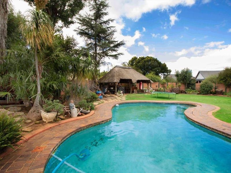 Outdoor pool area featuring a swimming pool with brick coping, a thatched lapa, and a spacious lawn garden.