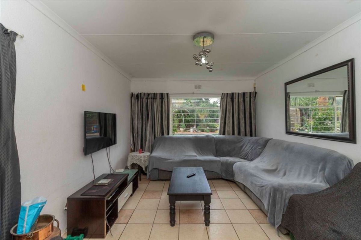 A functional living room featuring tiled flooring, a large window with security bars, and a central ceiling light fixture.