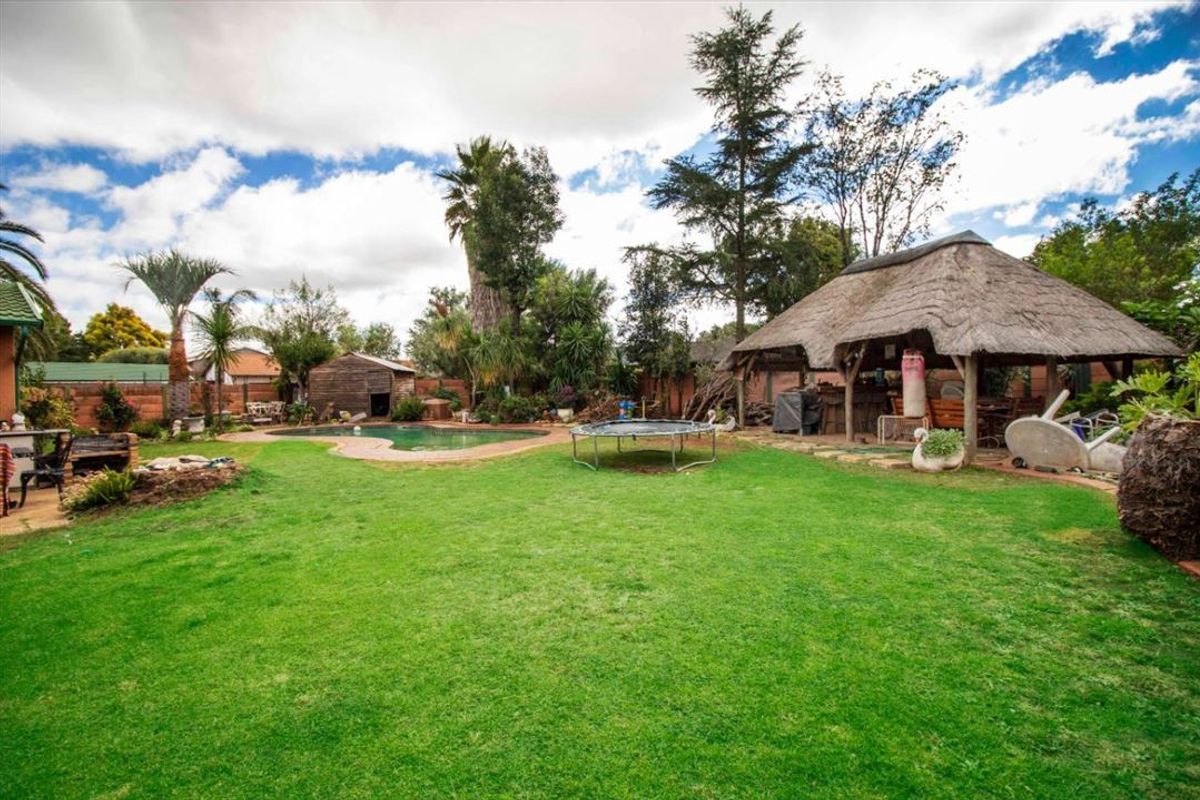 Spacious backyard featuring a swimming pool, a traditional thatch lapa entertainment area, and established garden landscaping.