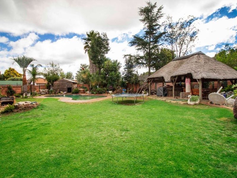 Spacious backyard featuring a swimming pool, a traditional thatch lapa entertainment area, and established garden landscaping.