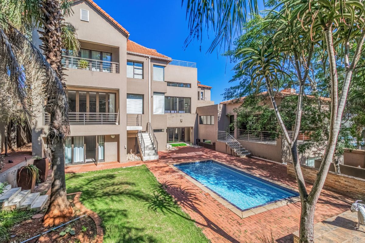 Rear view of a multi-story house featuring a swimming pool, brick-paved patio area, landscaped garden, and multiple balconies.