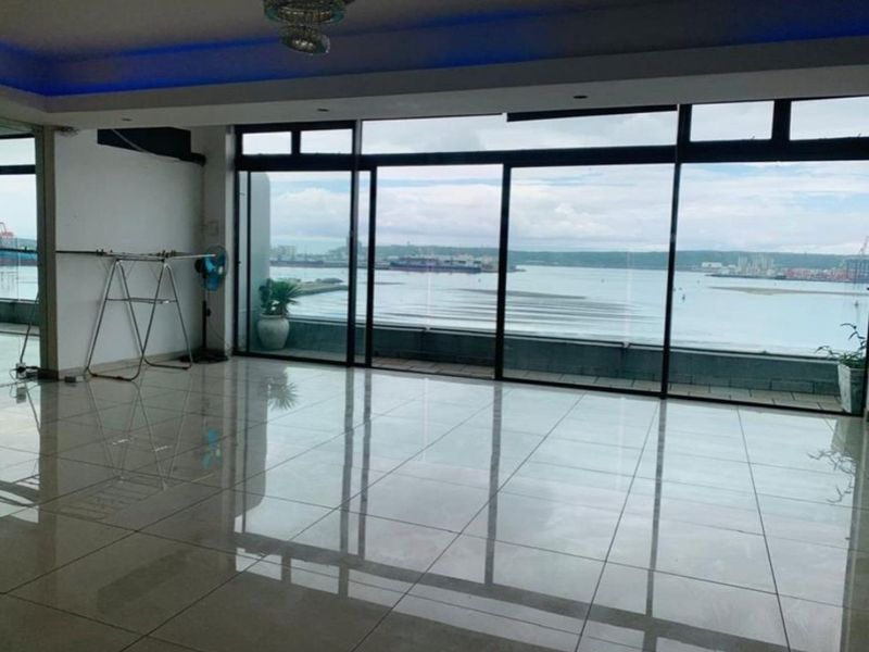 Spacious open-plan living area featuring large sliding glass doors that open onto a balcony with expansive harbour and sea views.