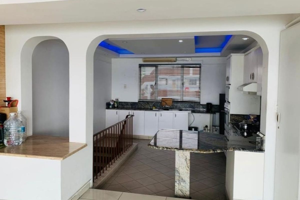 A functional kitchen featuring granite countertops, built-in cabinetry, and integrated appliances, with a unique arched opening overlooking a staircase.