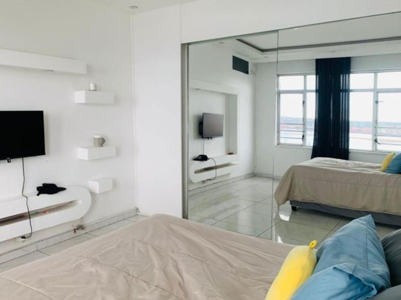 A bright bedroom featuring large built-in mirrored wardrobes, tiled flooring, recessed ceiling lighting, and integrated wall shelving units.