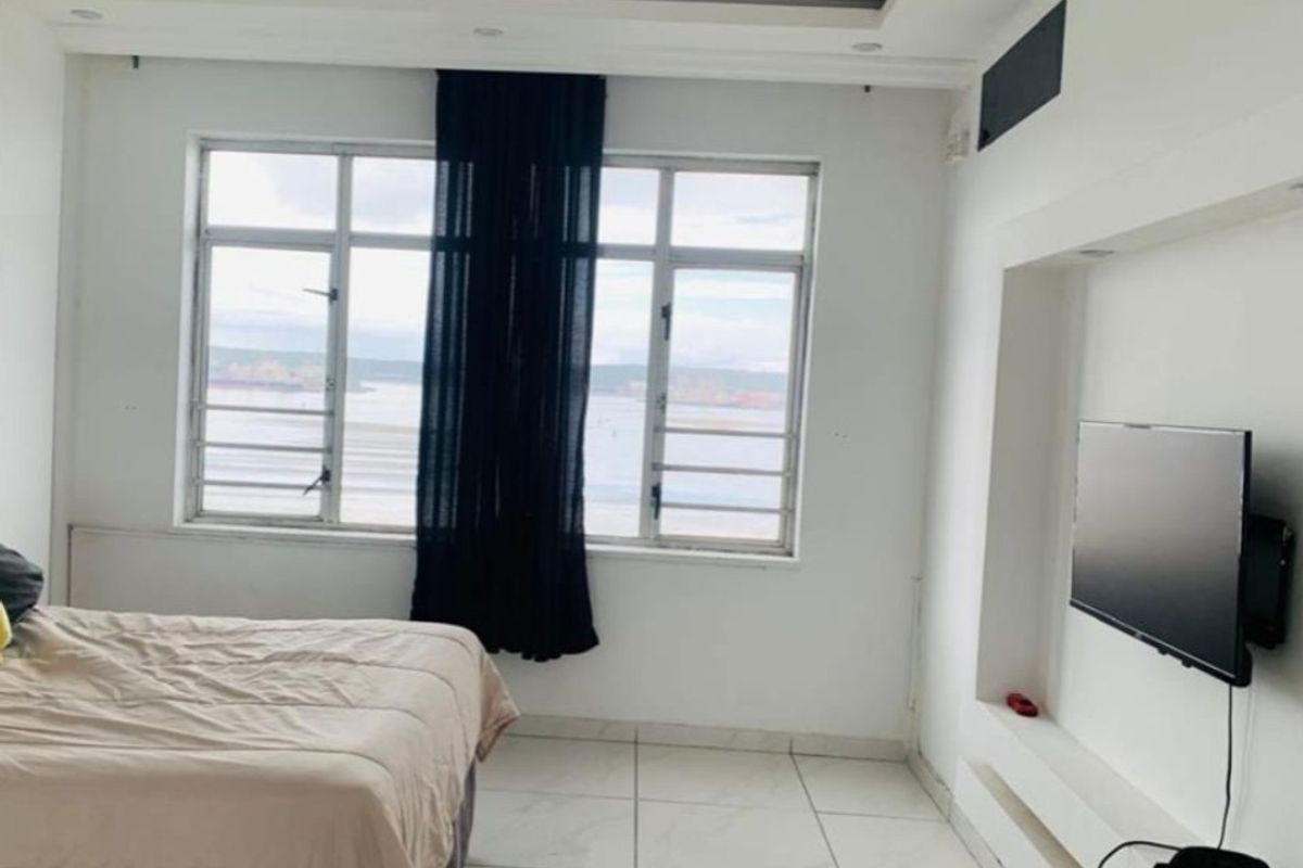 A bright bedroom featuring tiled flooring, a built-in media niche, and large windows with views, offering a clean and modern living space.