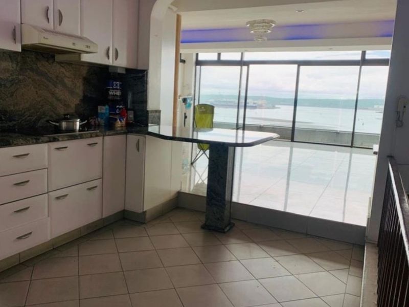 Open plan kitchen featuring granite countertops and a breakfast bar, flowing into a living area with expansive ocean views through large sliding glass doors.