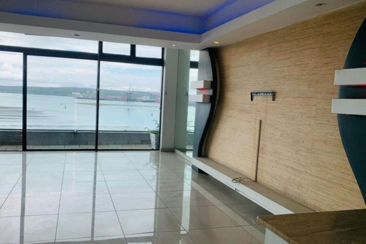 Spacious living area featuring polished tile floors, a modern built-in feature wall with integrated lighting, and large sliding doors offering expansive water views.