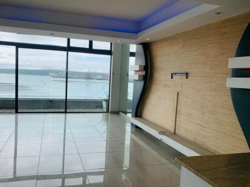 Spacious living area featuring polished tile floors, a modern built-in feature wall with integrated lighting, and large sliding doors offering expansive water views.