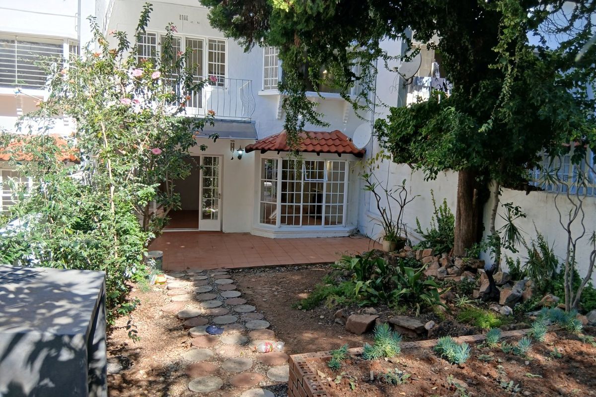 Rear view of the apartment featuring a private garden, terracotta tiled patio, bay window, and a small balcony on the upper level.