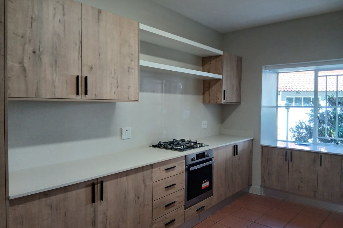 Modern kitchen featuring light wood-grain cabinetry, stone countertops, built-in gas hob and oven, and tiled flooring with ample natural light.