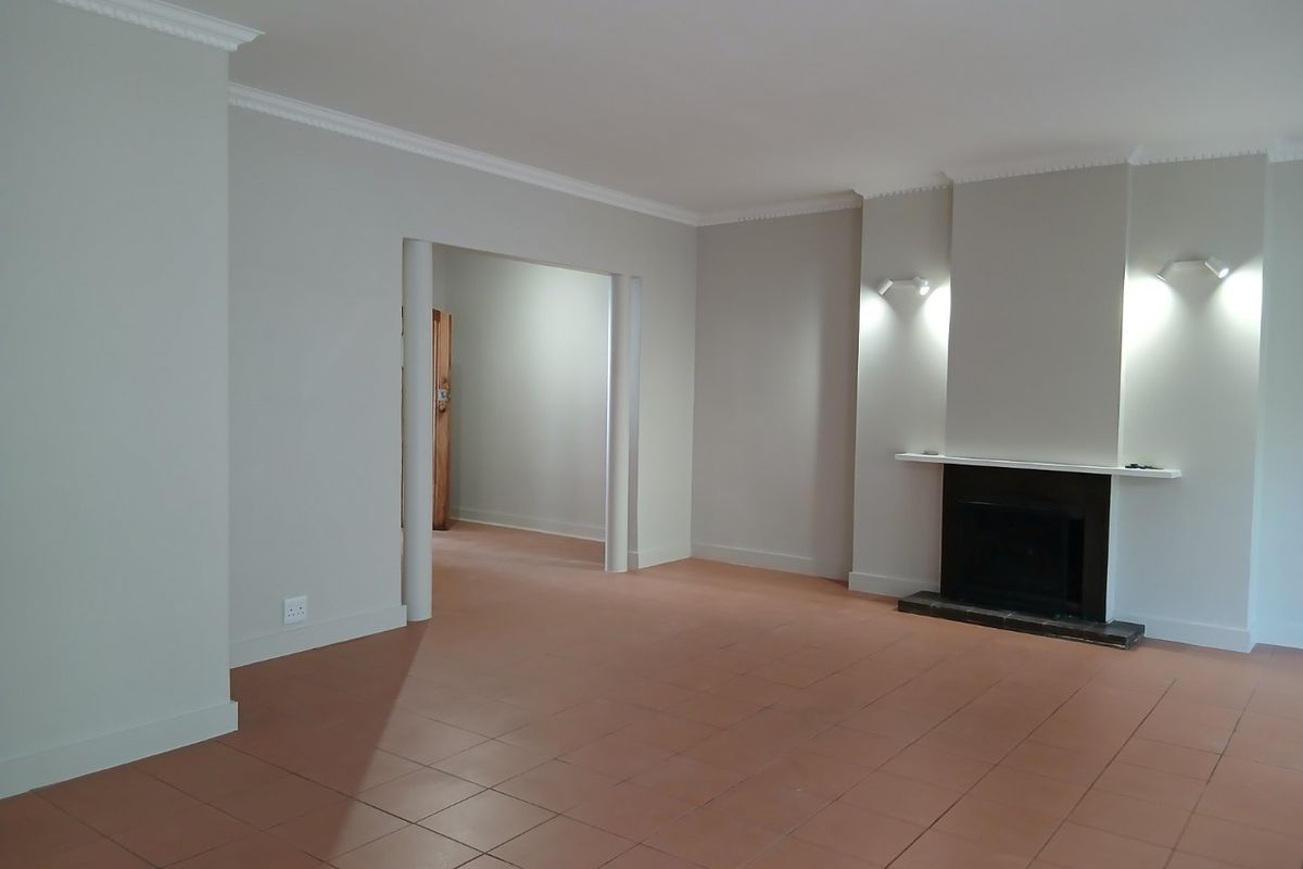 Spacious, empty living room featuring neutral walls, tiled flooring, crown molding, and a built-in fireplace with accent wall lighting.
