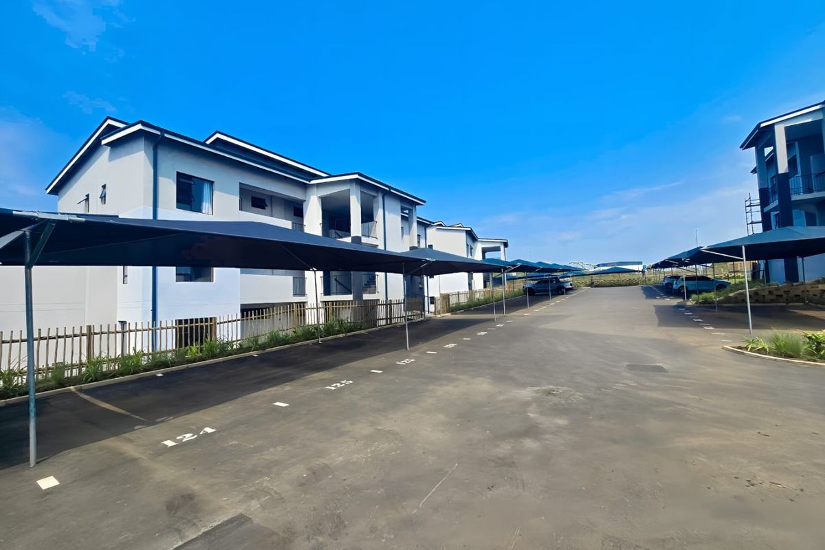 Modern apartment complex exterior featuring paved parking area with dedicated shade cloth carports and well-maintained building facades.