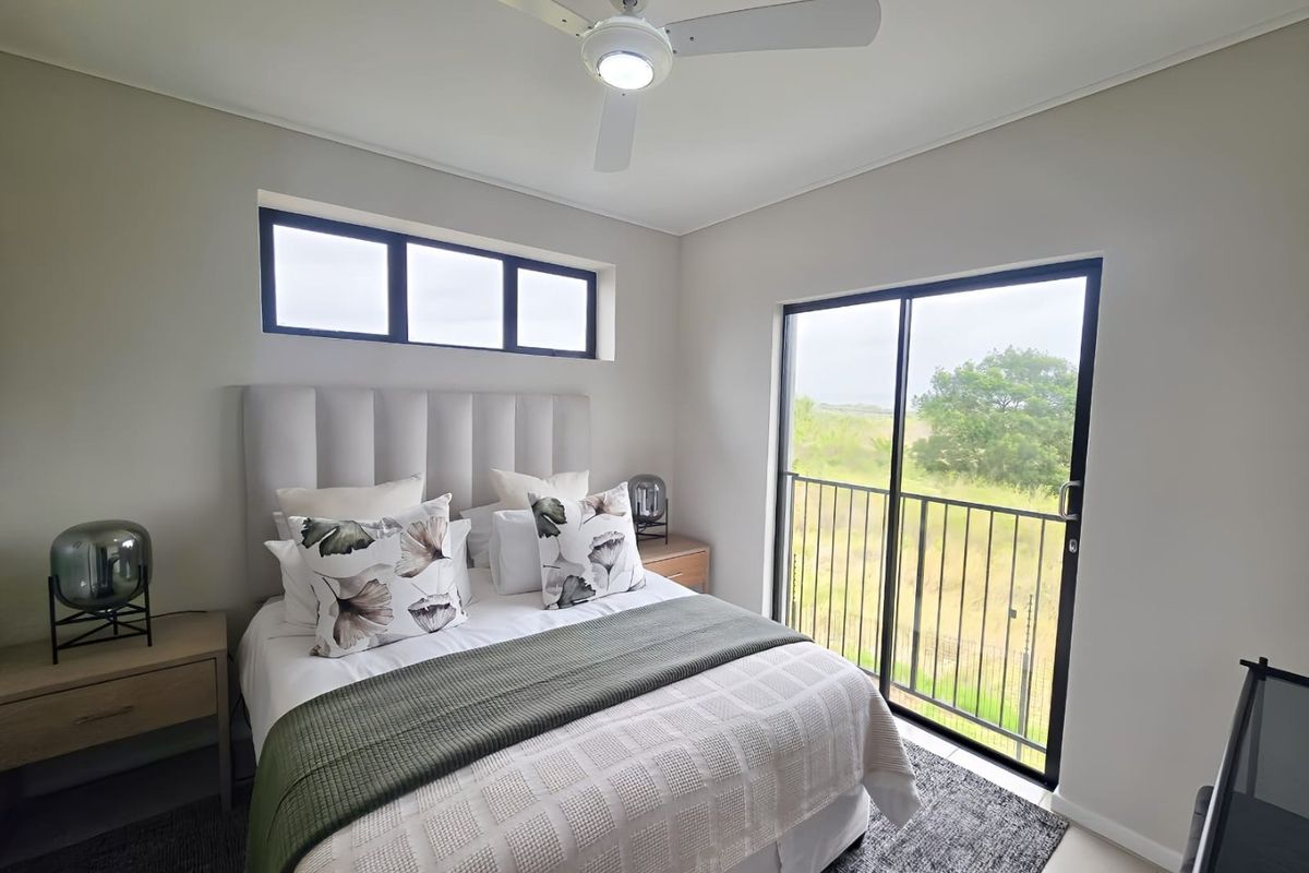 A well-lit bedroom featuring a ceiling fan, tiled flooring, and a sliding glass door that opens to a balcony with scenic views.