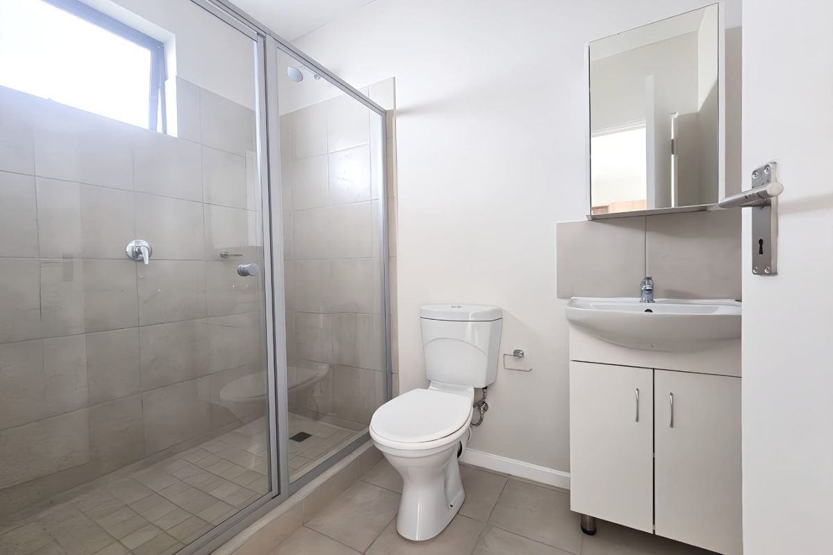 A clean and functional bathroom featuring a walk-in shower with glass enclosure, a modern vanity with integrated basin, and neutral ceramic tiling throughout.