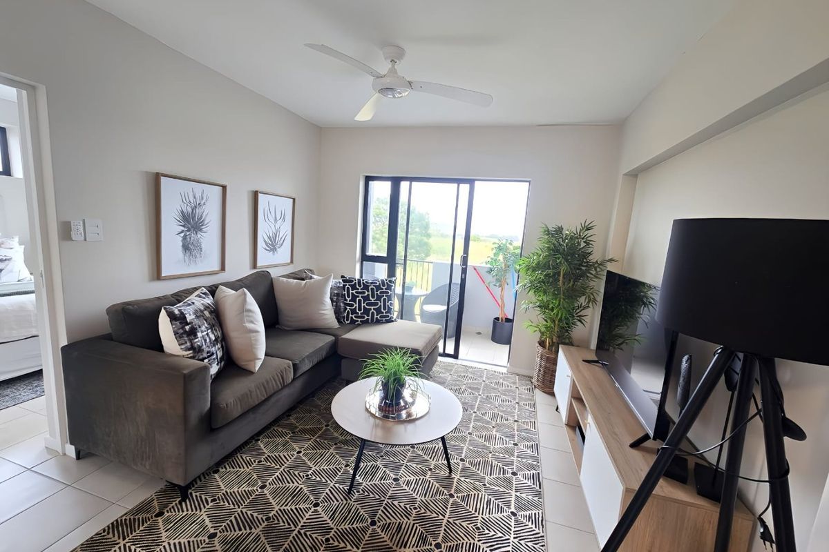 A well-maintained living room featuring tiled flooring, a ceiling fan, and sliding glass doors that provide access to an outdoor balcony area.